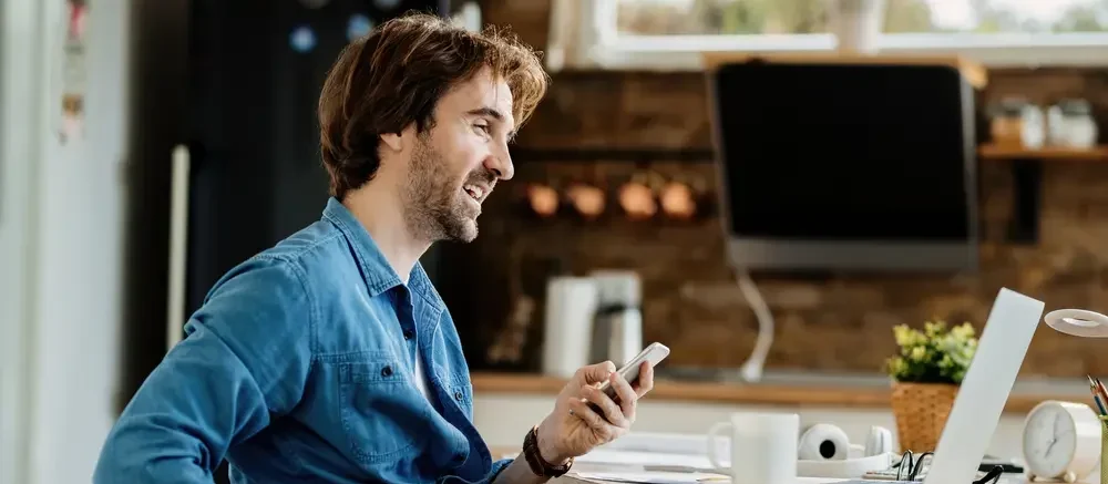 The image features a young, happy businessman in a wheelchair, working from home and texting on a cell phone. This scene represents the context of an ADA (Americans with Disabilities Act) Website Audit, highlighting the importance of ensuring website accessibility for individuals with disabilities, including those who work remotely.