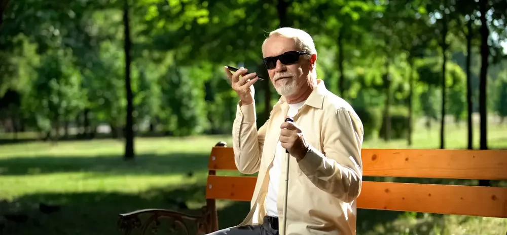 A blind man is shown listening attentively to his phone, highlighting the importance of Audio Description Services. This image emphasizes the role of technology in providing accessible content for visually impaired individuals.