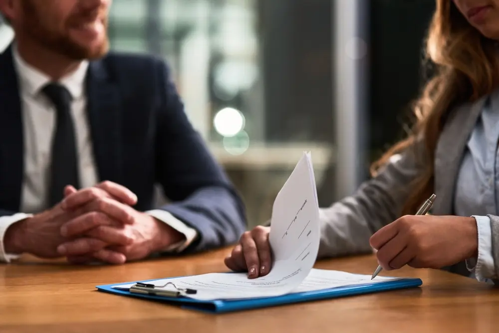 Image showing business professionals in a night office, signing contracts and legal paperwork. A lawyer woman's hands are seen managing policy, compliance, and partnership agreements.