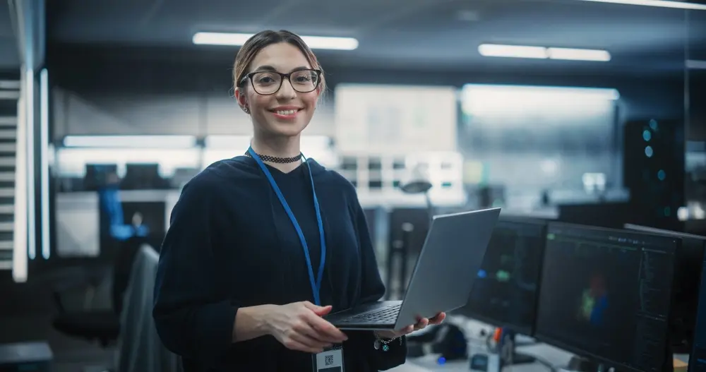 A portrait of an attractive, empowered multiethnic woman looking at the camera with a charming smile. She is depicted as a businesswoman at work, an Information Technology Manager, or a Software Engineering Professional. This image is contextualized within Functional Testing Services, illustrating the expertise and confidence of women in the field of IT.