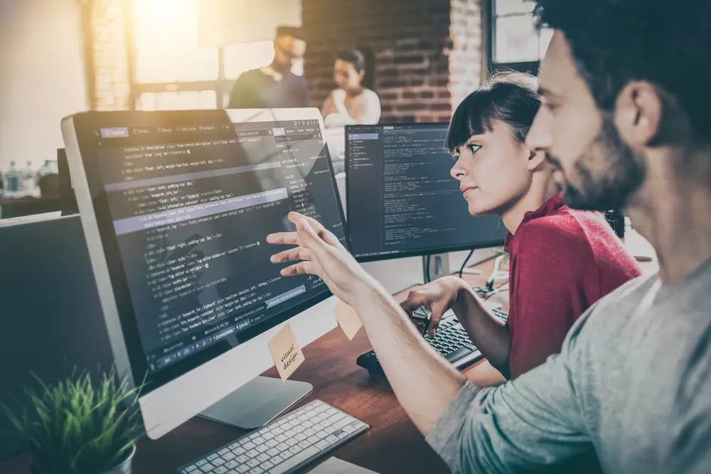 A programmer is shown working in a software development company office, focusing on developing programming and coding technologies for website design. This image is contextualized within Load Testing Services, illustrating the importance of optimizing performance through rigorous load testing.
