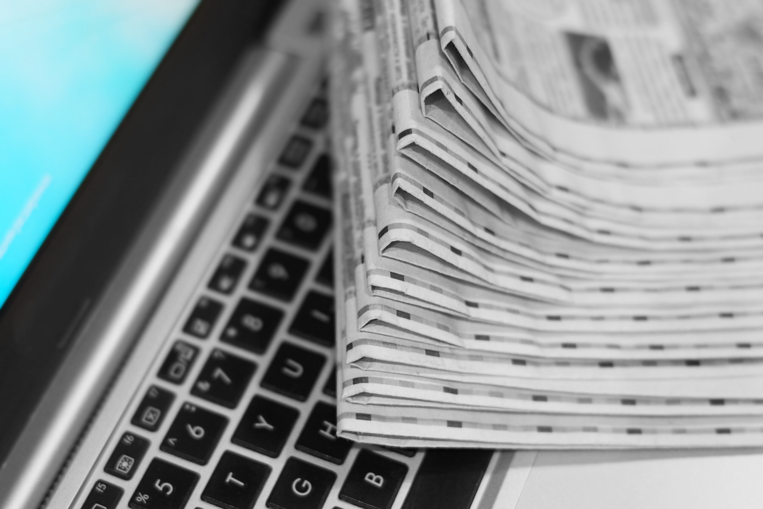 stack of newspapers sitting on top of a macbook laptop