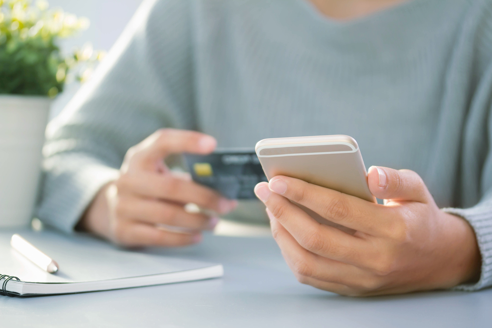 person in gray long-sleeve shirt using iPhone and holding credit card to make online purchase.