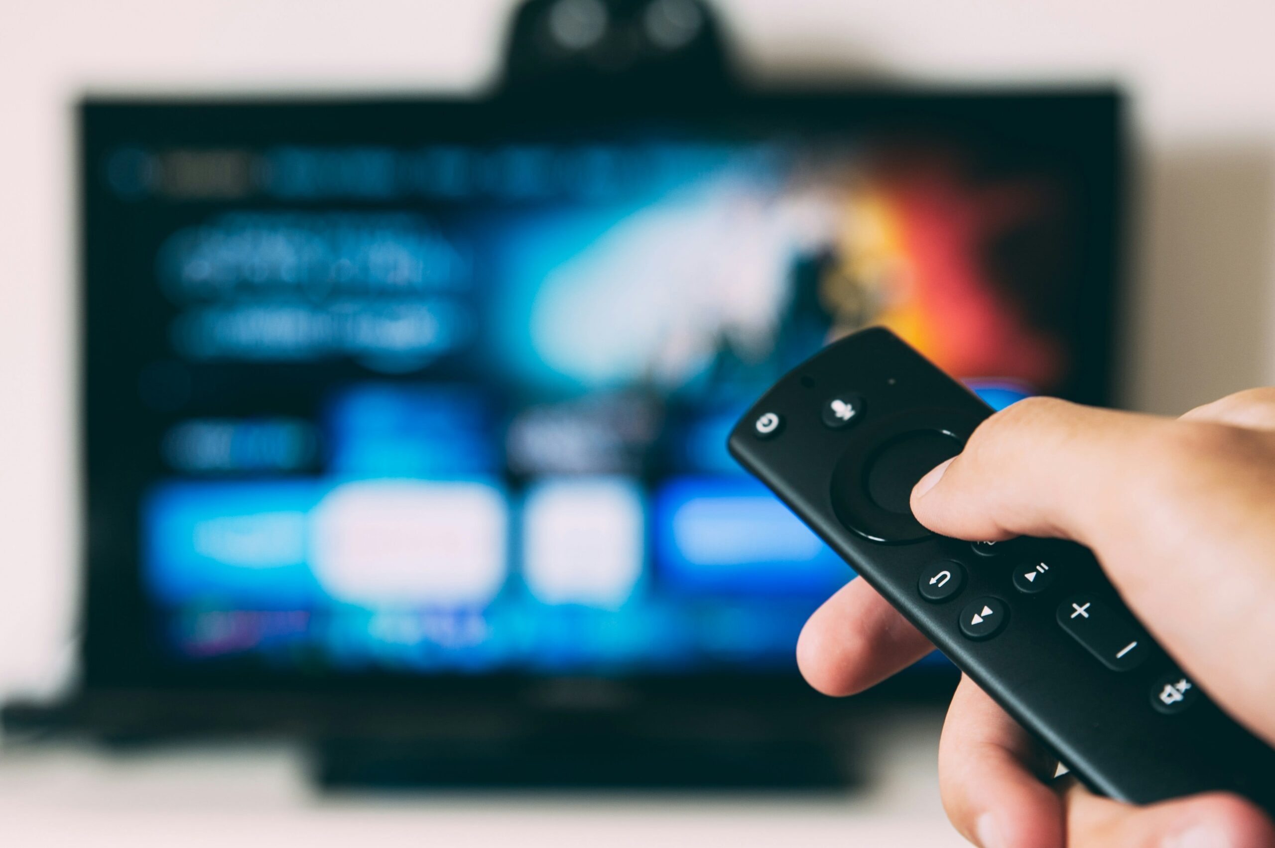 A person's hand holding a remote with a TV missing closed captions in the background
