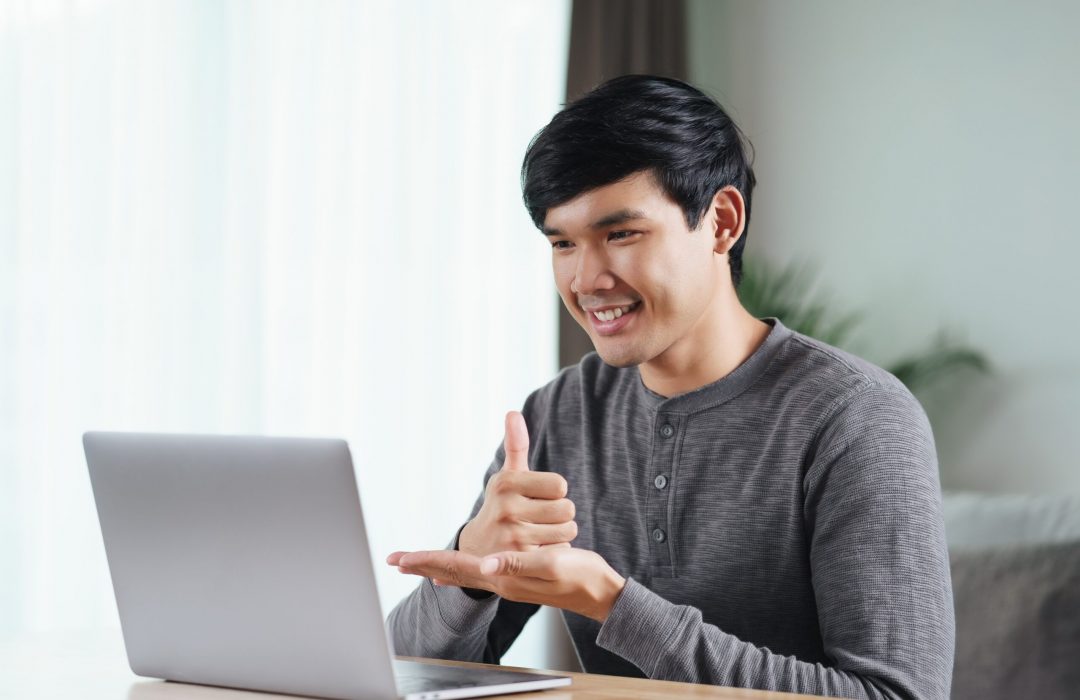 audio-description-services-allowing-young-asian-man-deaf-disabled-using-laptop-computer-online-video-conference-call-learning-communicating-sign-language-min young male is able to use laptop for videos after audio description services