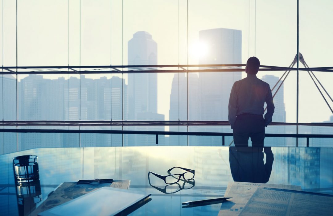 person in large office in high building looking out the window thinking about the future