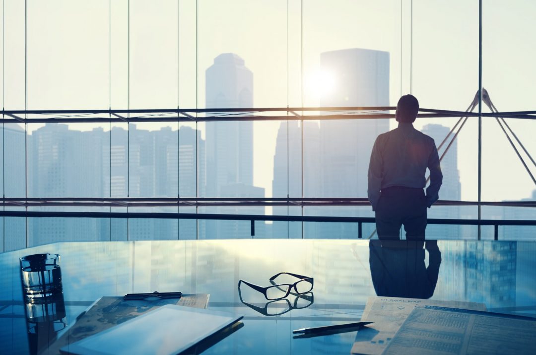 person in large office in high building looking out the window thinking about the future