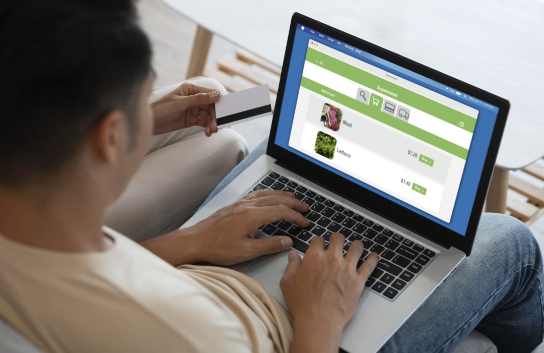 Couple shopping online using a laptop, with a credit card in hand and a grocery website open on the screen.