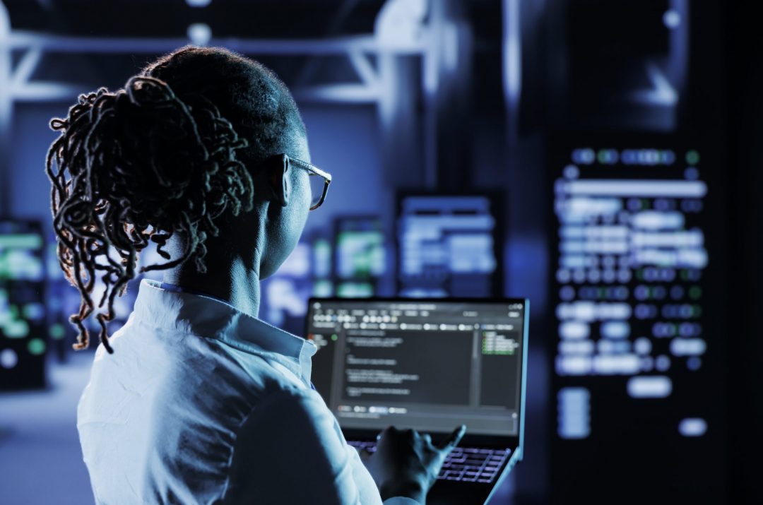 data-center-technician-runs-code-min business professional in data center analyzing code on a laptop