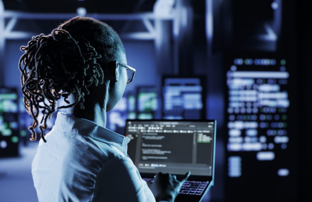 data-center-technician-runs-code-min business professional in data center analyzing code on a laptop