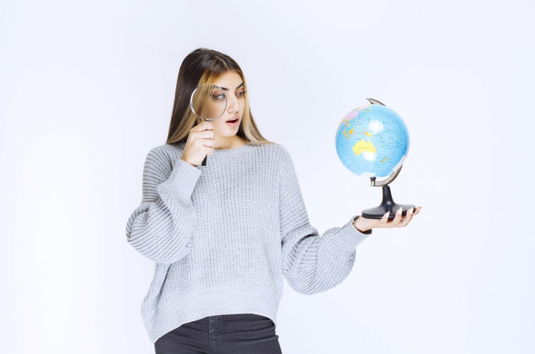 girl using magnifying glass to look at the earth on a small globe in her hand