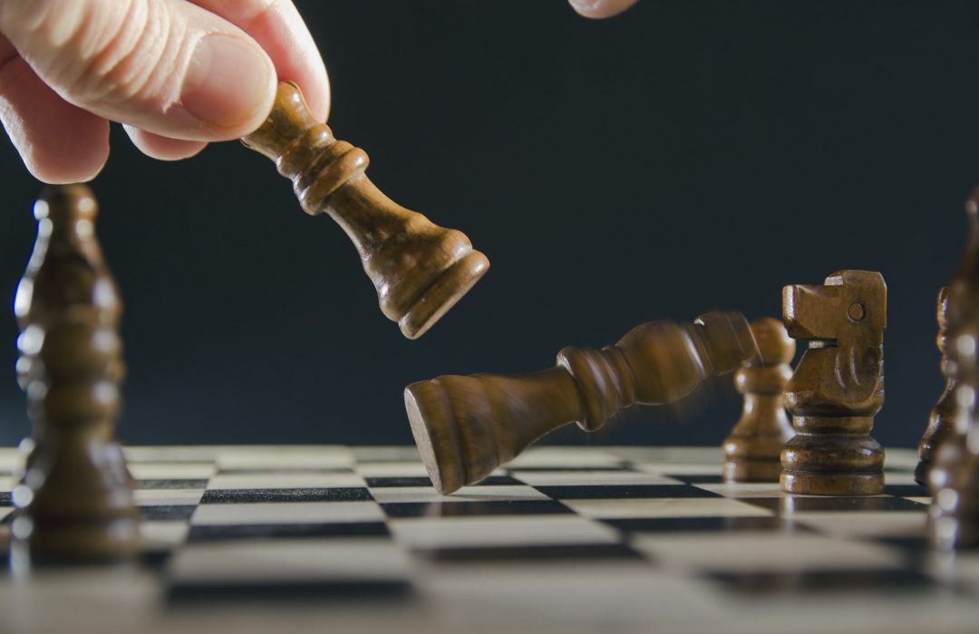 male-hand-moving-chess-piece-strategy-min person playing chess knocking over a competitor's piece