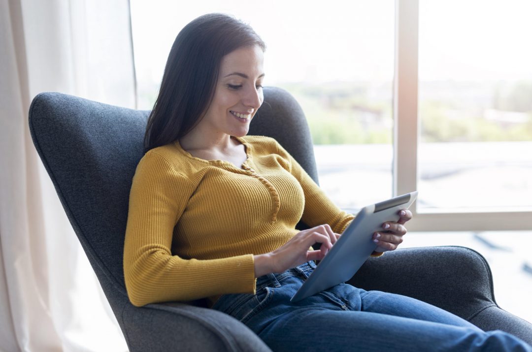 woman-sitting-chair-checking-tablet-min